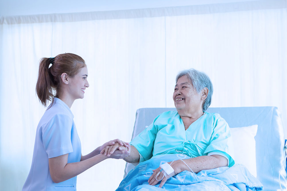 Nurse reassuring her patient on bed in hospital / healthcare medical concept