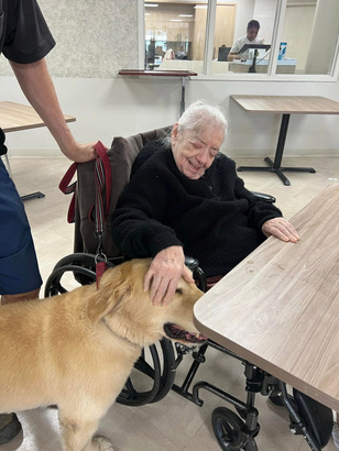 A resident at Saints Joachim & Anne smiling while petting a therapy dog