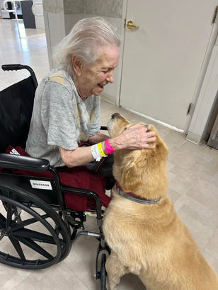 A resident laughing as she pets a therapy dog